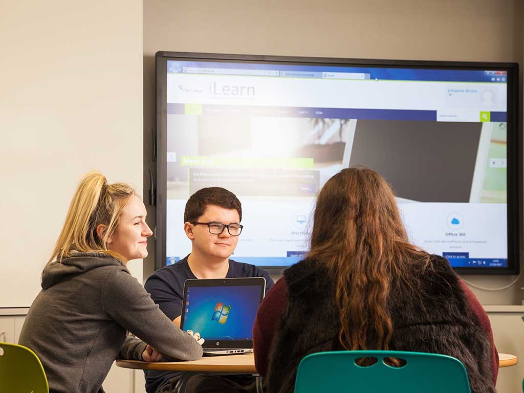 students working around a laptop smiling with screen in background