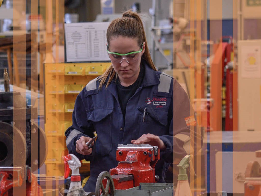 engineering student working on engineering equipment wearing goggles and overalls with orange stripes on top of image