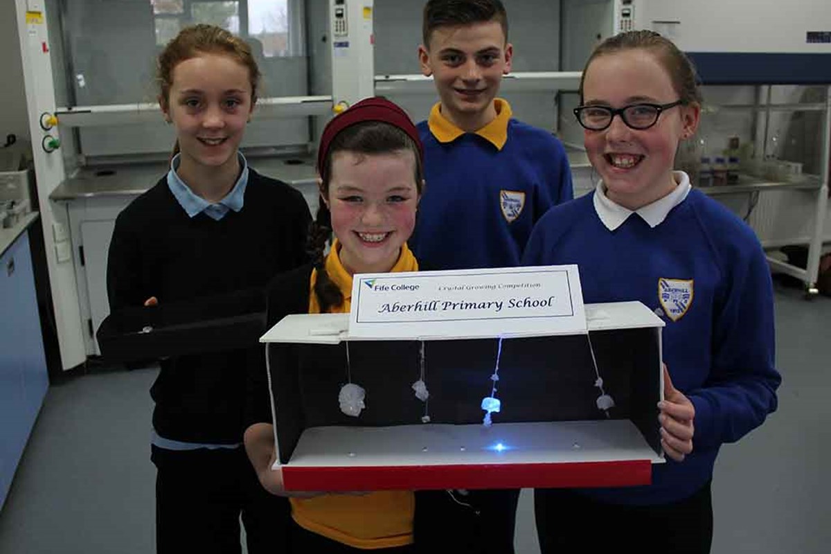 Four school pupils holding box with hanging crystals