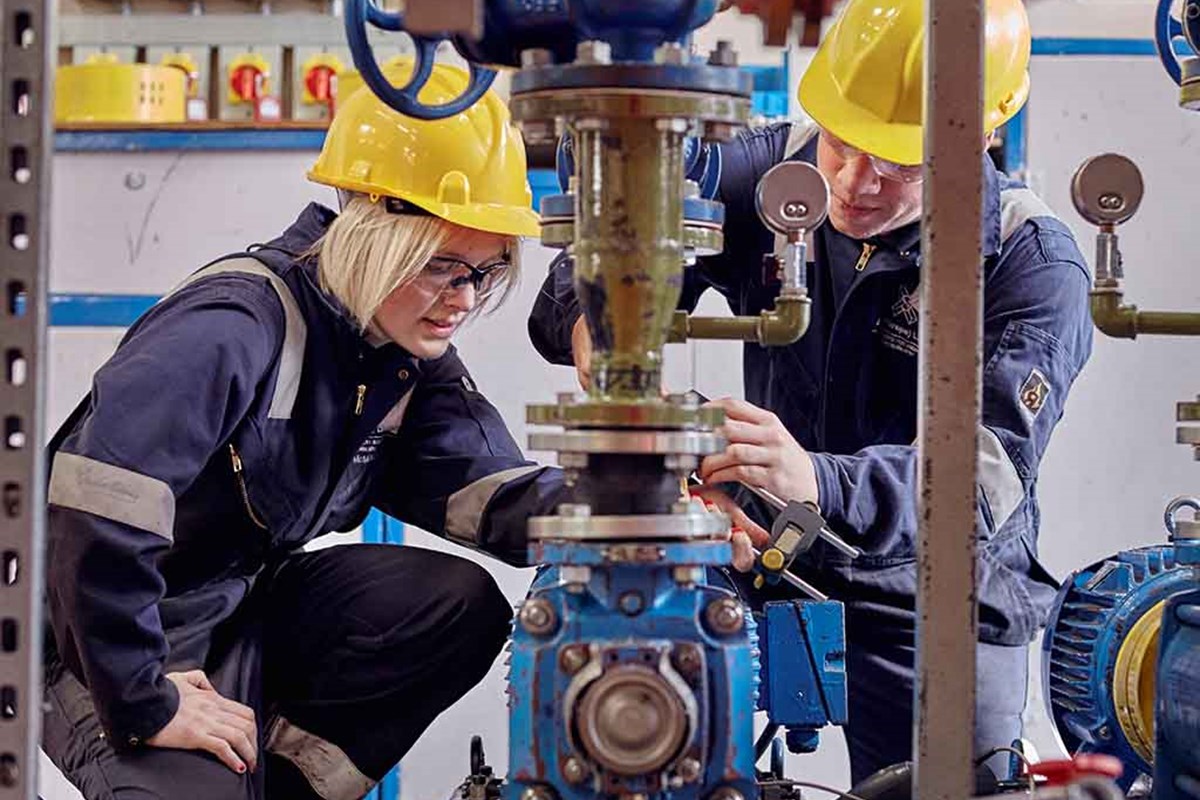 two engineer students working on equipment wearing helmet and blue overall