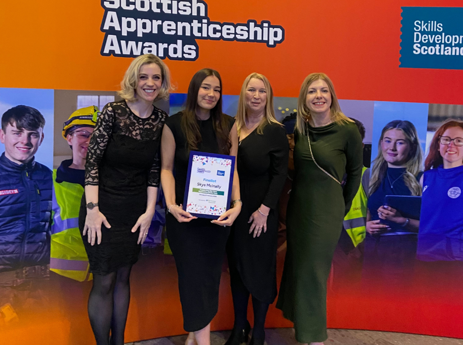 Four women pose at the Scottish Apprenticeship Awards, with finalist holding her certificate in front of the event backdrop.