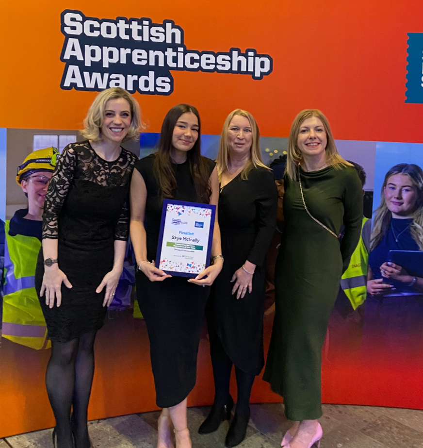 Four women pose at the Scottish Apprenticeship Awards, with finalist holding her certificate in front of the event backdrop. Four women pose at the Scottish Apprenticeship Awards, with finalist holding her certificate in front of the event backdrop.