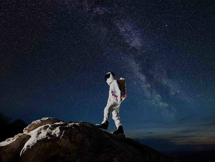 astronaut on top of rock with night sky in background