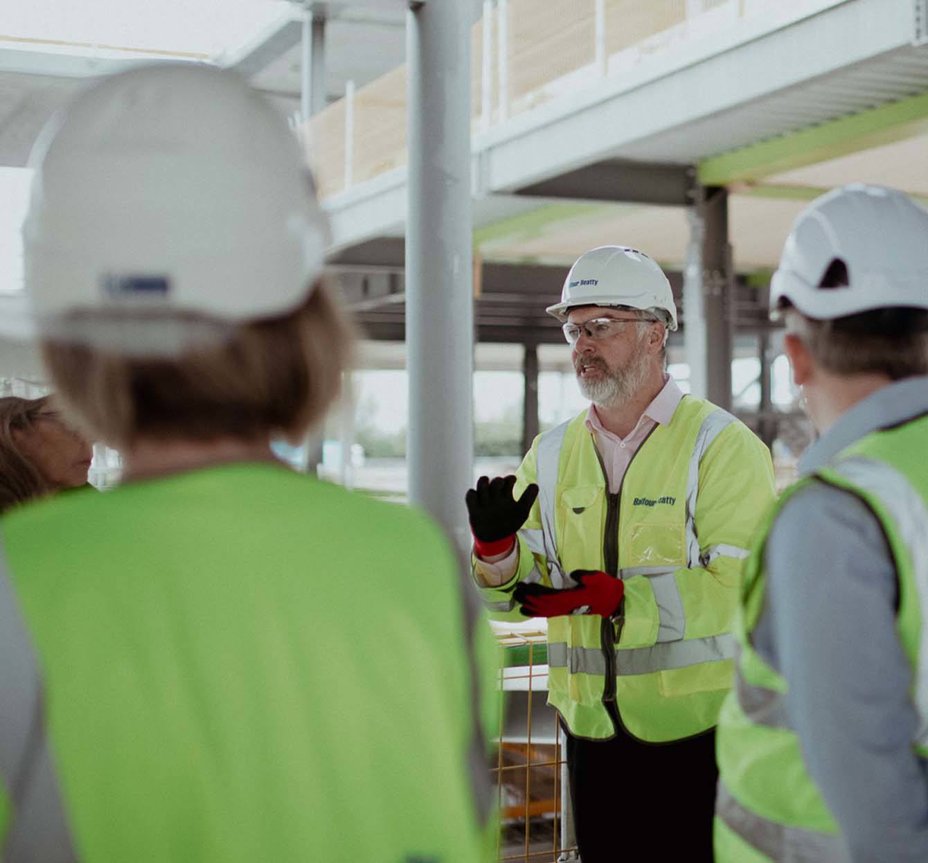 people with hard hats on, high vis jackets listening to man talking 