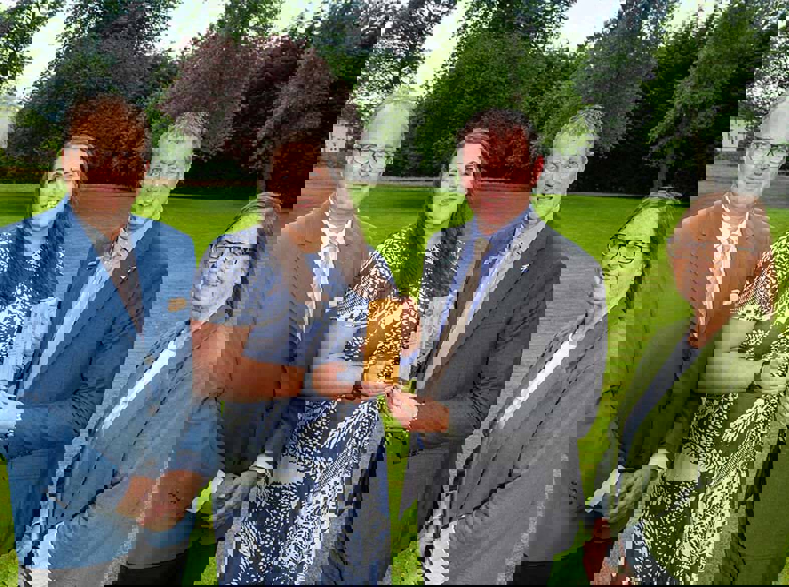 Four people standing on grass holding a wooden award Four people standing on grass holding a wooden award