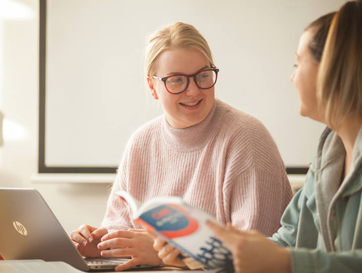 two female students smiling working on laptop